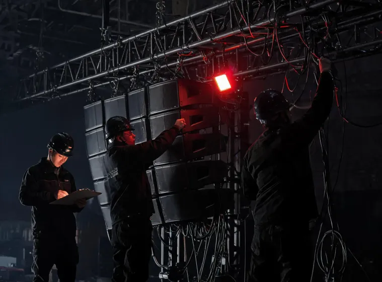 Stage crew verifying speaker rigging and cable paths before an event
